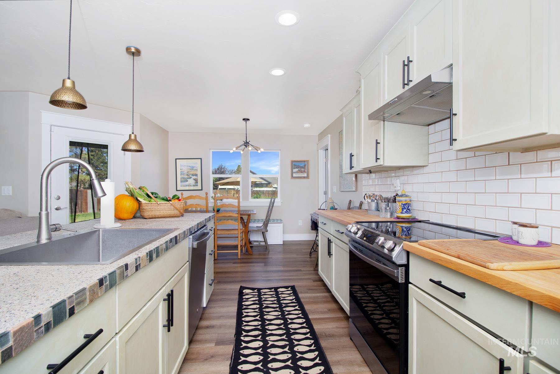 Kitchen with stainless steel appliances, decorative light fixtures, under cabinet range hood, light wood-style flooring, and recessed lighting
