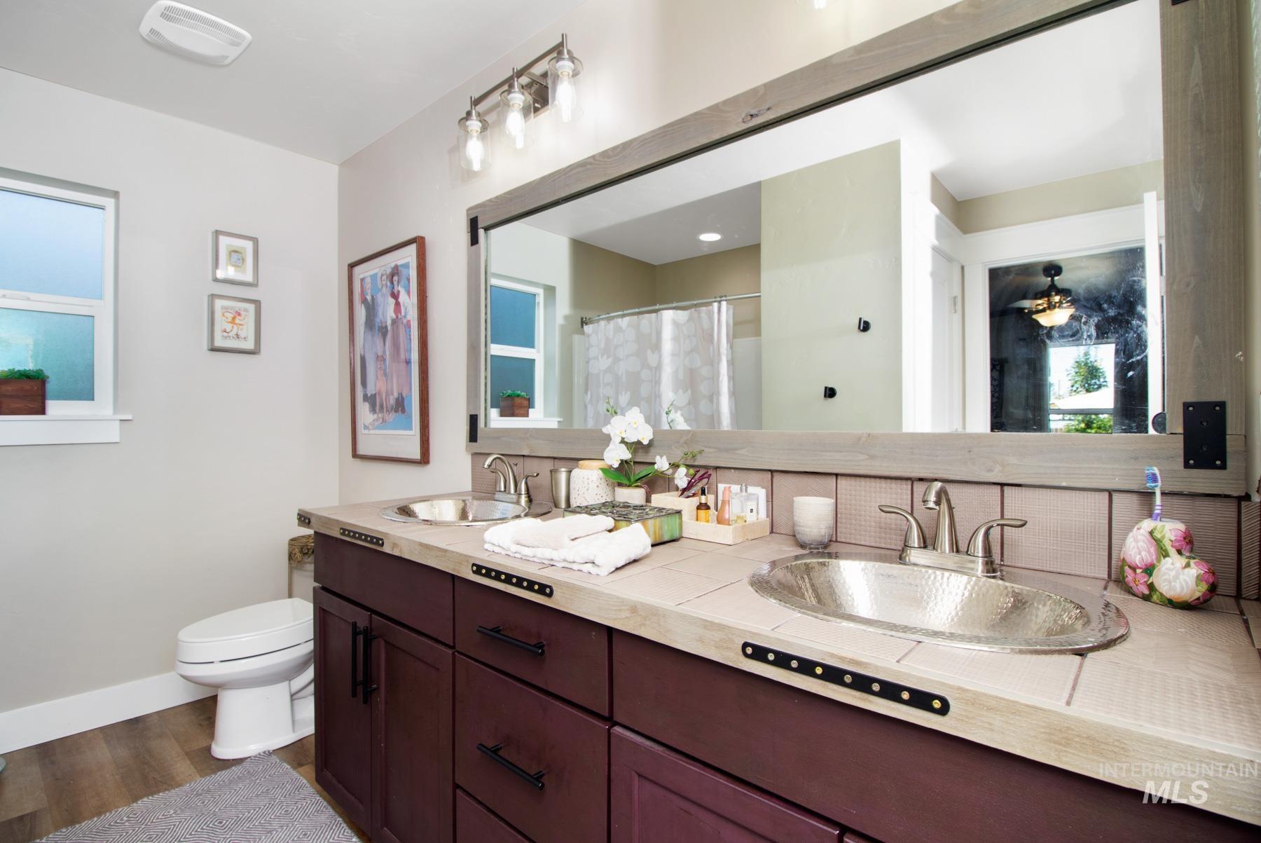 Full bath with curtained shower, double vanity, and dark wood-style floors