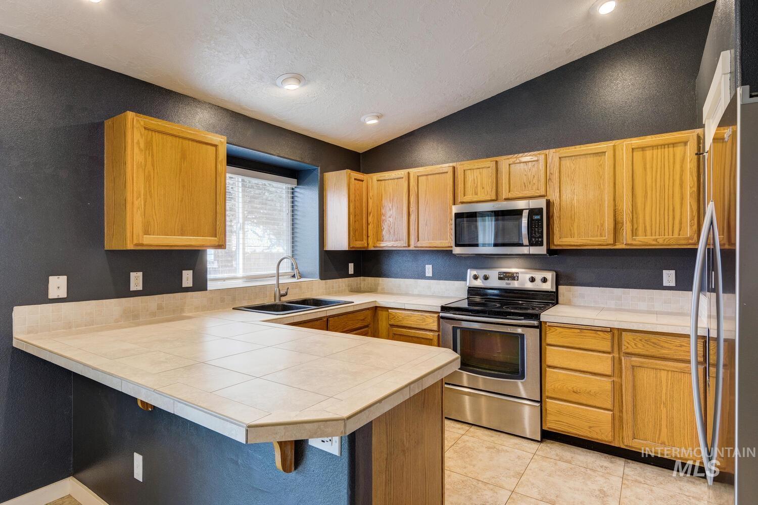 Kitchen with appliances with stainless steel finishes, a peninsula, lofted ceiling, a kitchen bar, and tile countertops