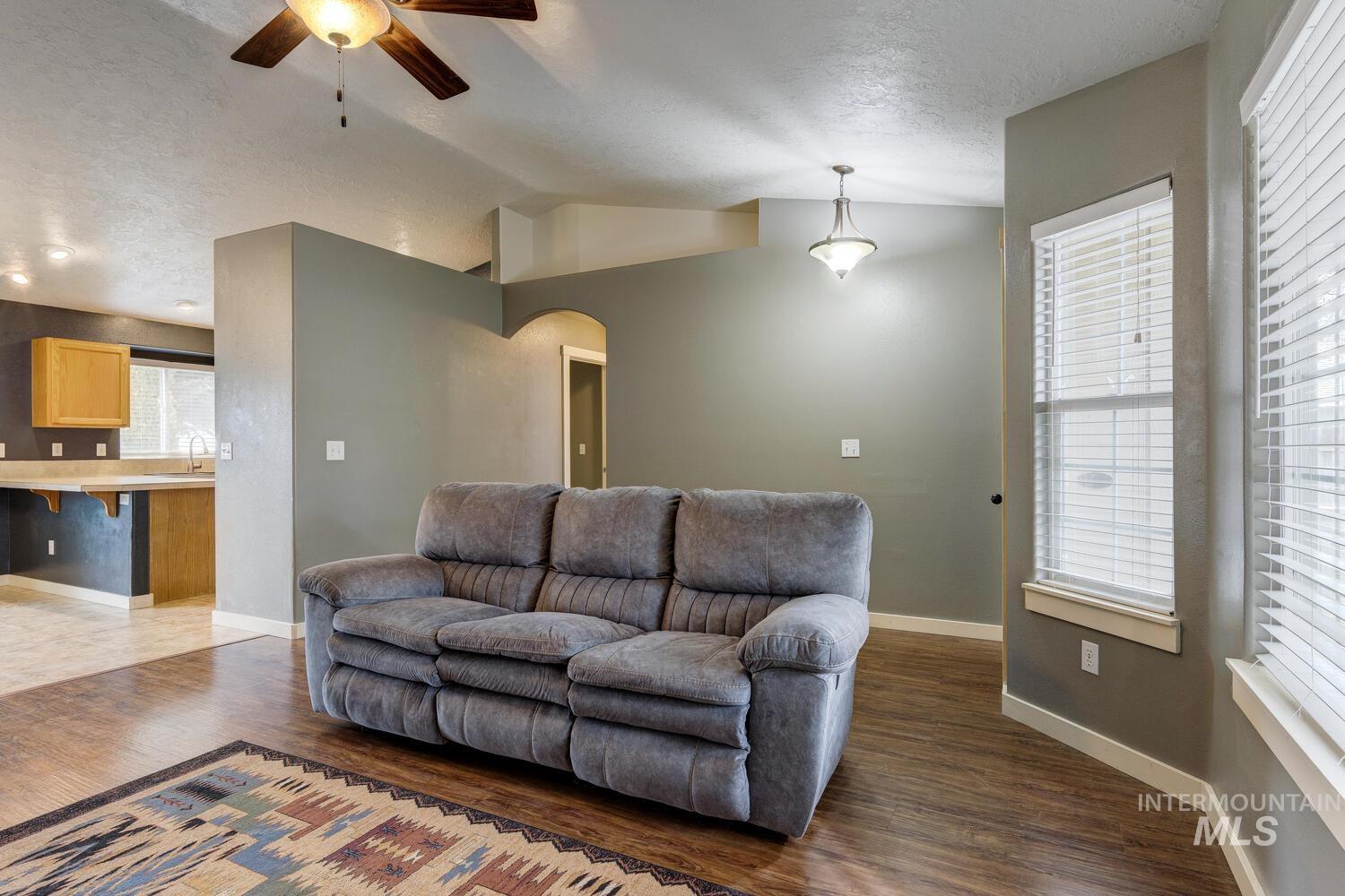 Living room featuring vaulted ceiling, wood finished floors, a textured ceiling, a ceiling fan, and arched walkways