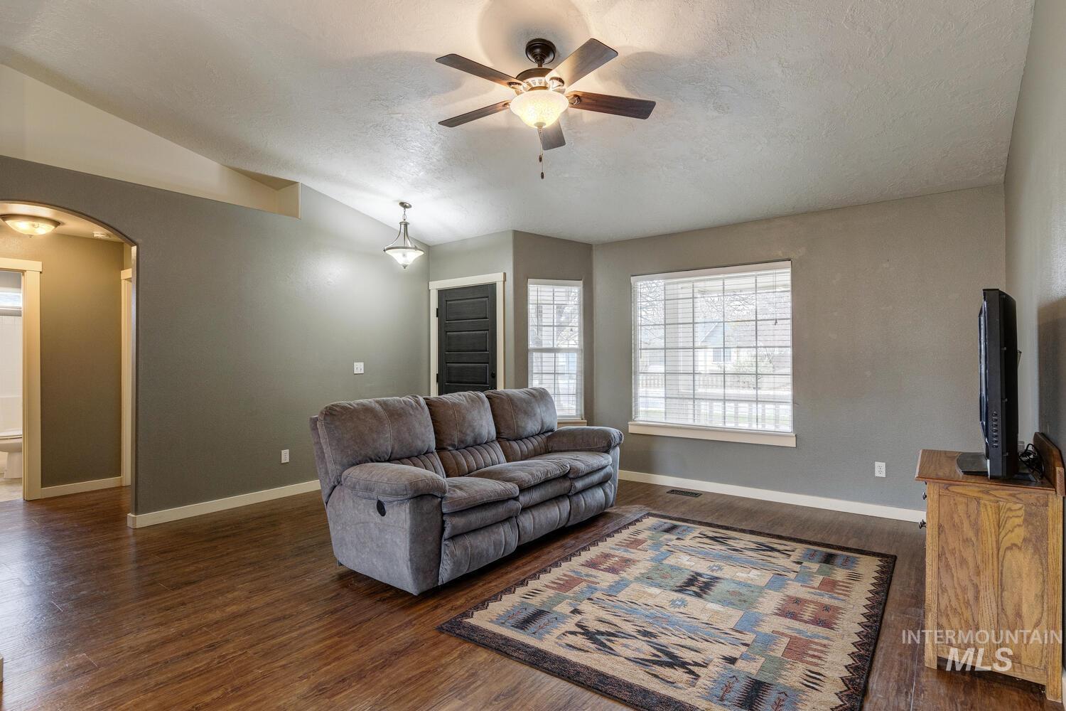 Living room with arched walkways, vaulted ceiling, dark wood-type flooring, a textured ceiling, and ceiling fan