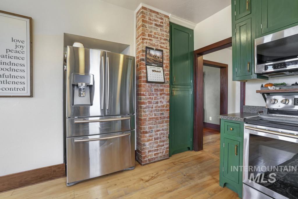 Kitchen featuring green cabinetry, appliances with stainless steel finishes, light wood-style floors, and dark stone countertops