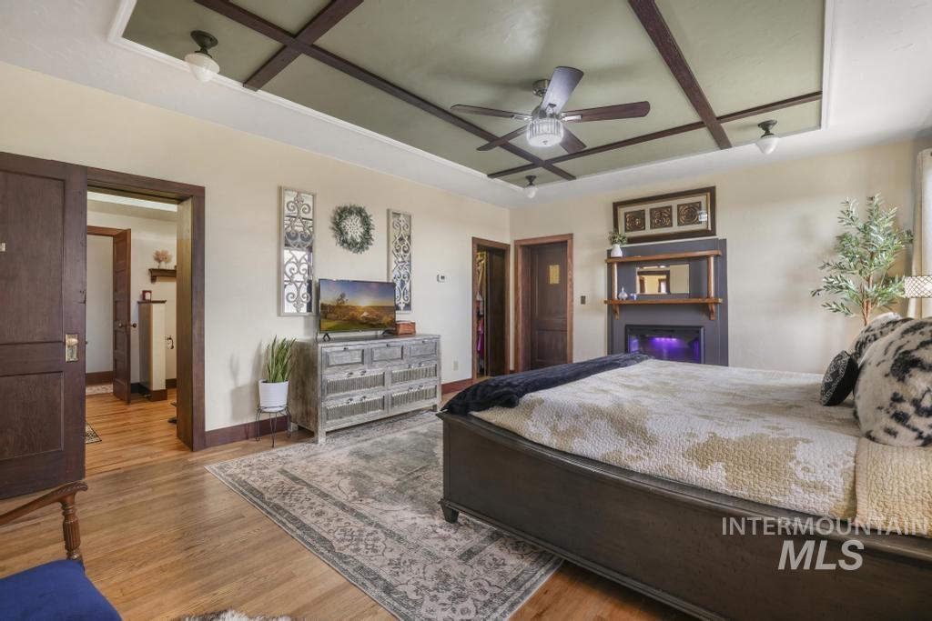 Bedroom featuring wood finished floors, a ceiling fan, coffered ceiling, and a lit fireplace