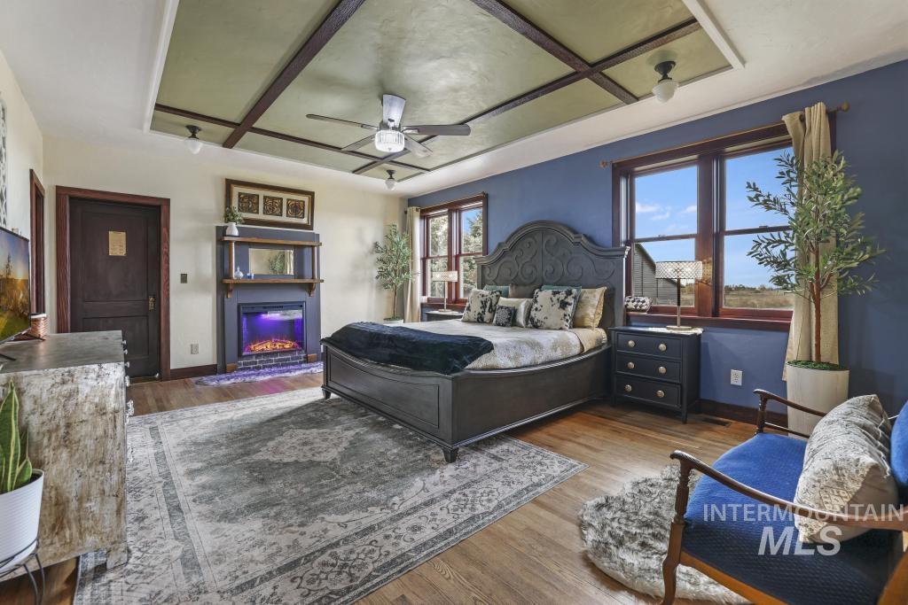 Bedroom with wood finished floors, a glass covered fireplace, and ceiling fan