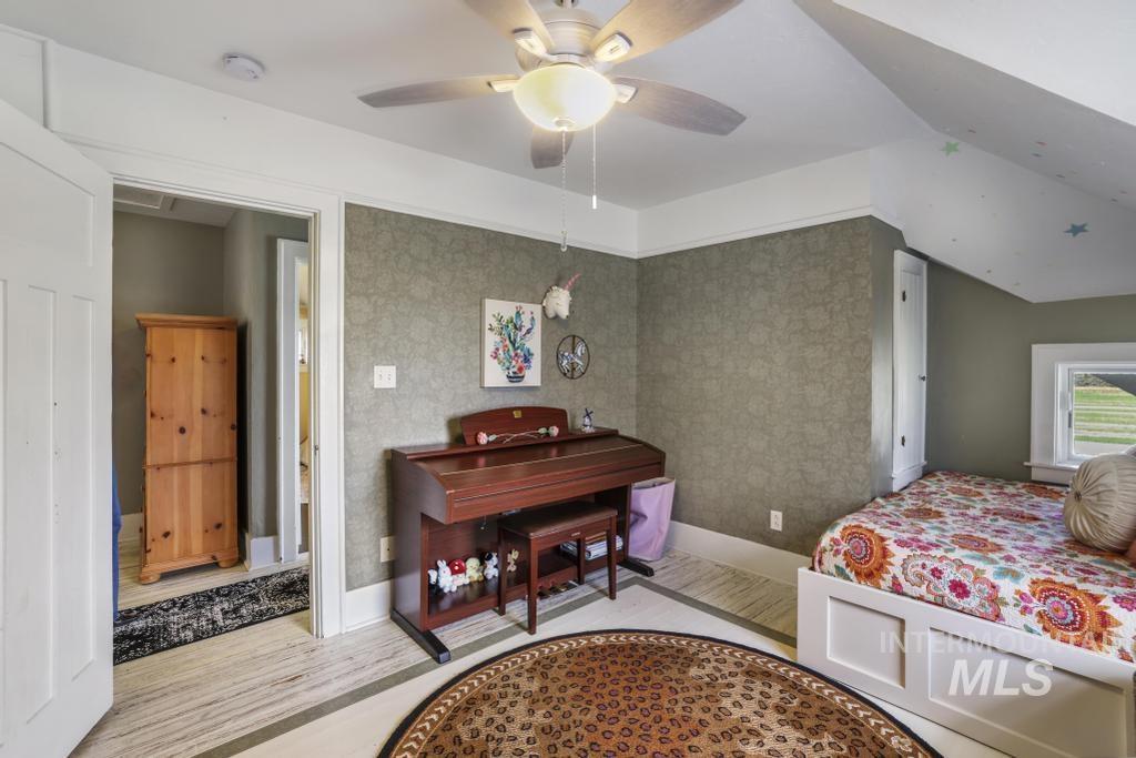 Bedroom with wallpapered walls, wood finished floors, a ceiling fan, and lofted ceiling