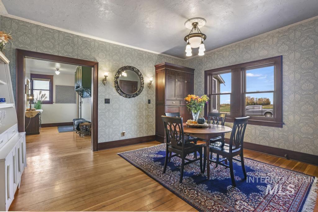 Dining space featuring plenty of natural light, light wood finished floors, ornamental molding, wallpapered walls, and a textured ceiling