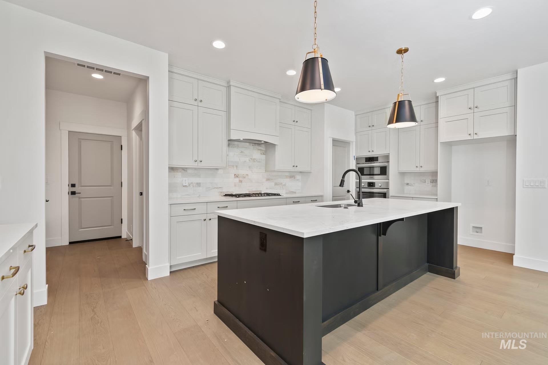 Kitchen with decorative backsplash, white cabinets, a kitchen island with sink, light wood-type flooring, and recessed lighting