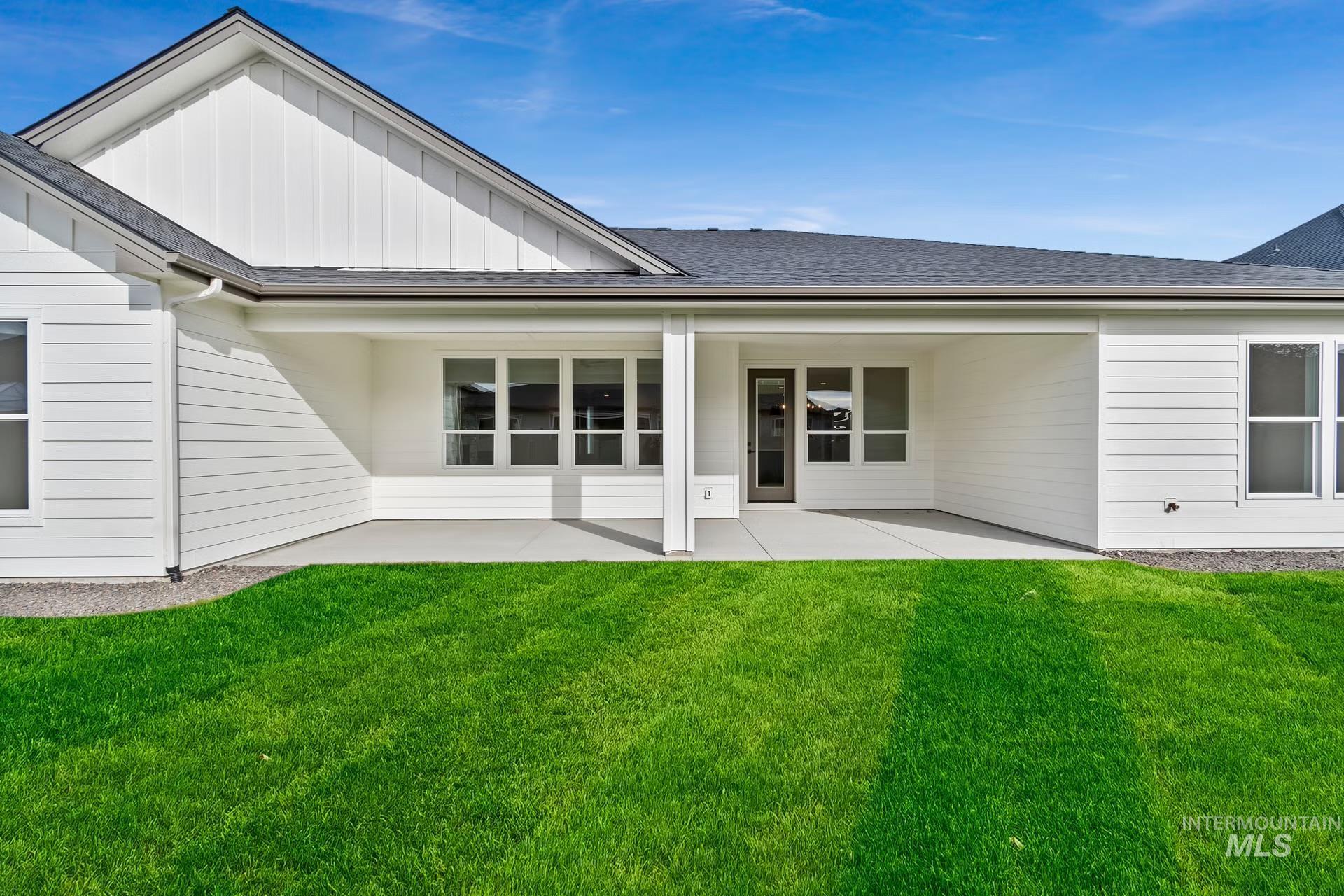 Back of property featuring board and batten siding, a patio area, roof with shingles, and a yard