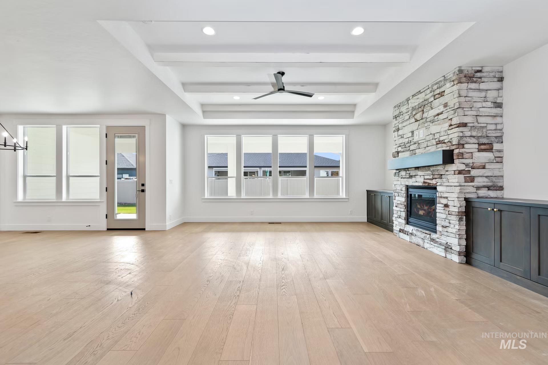 Unfurnished living room with a raised ceiling, light wood-type flooring, a stone fireplace, ceiling fan, and a chandelier