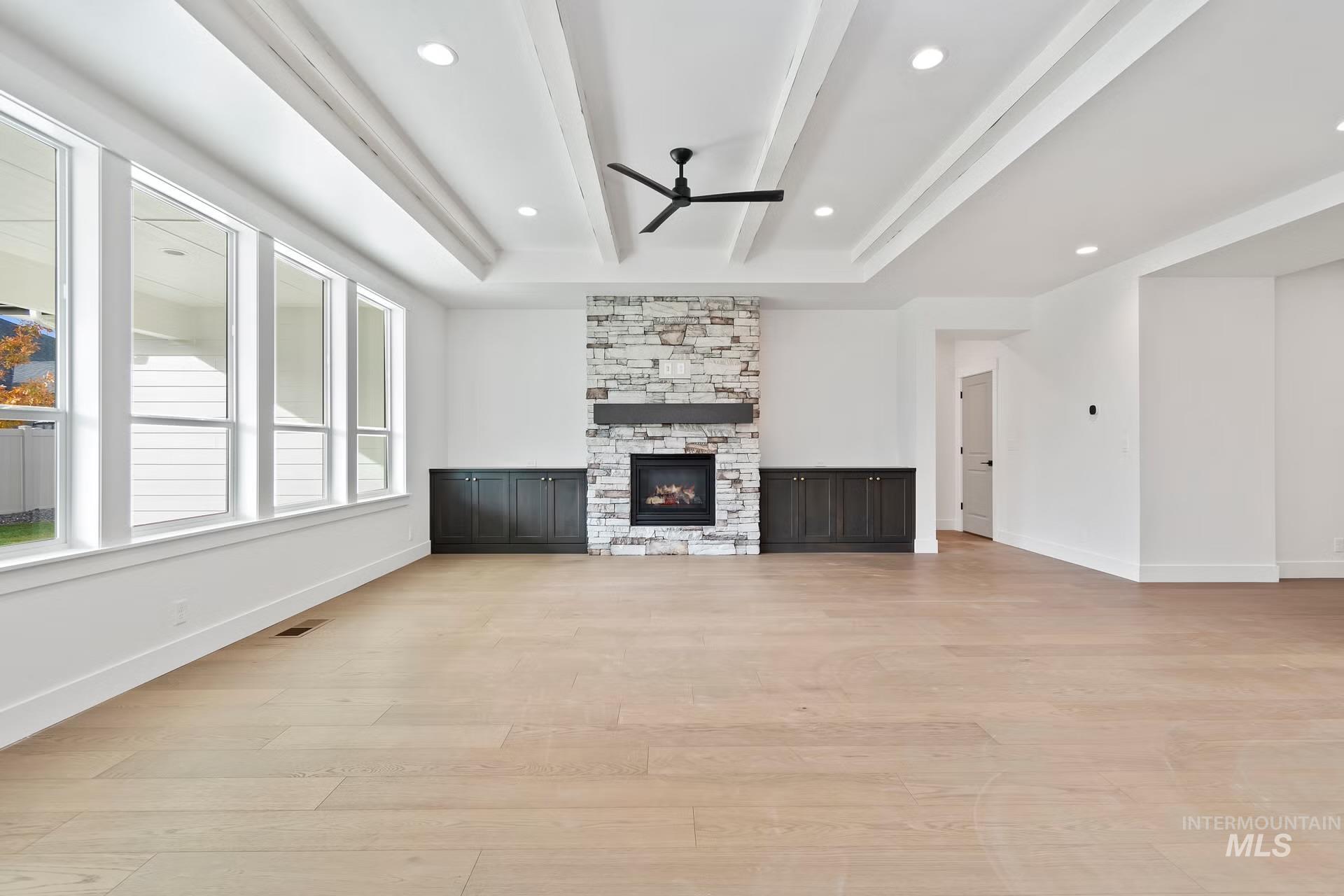 Unfurnished living room with beamed ceiling, ceiling fan, light wood finished floors, a stone fireplace, and recessed lighting