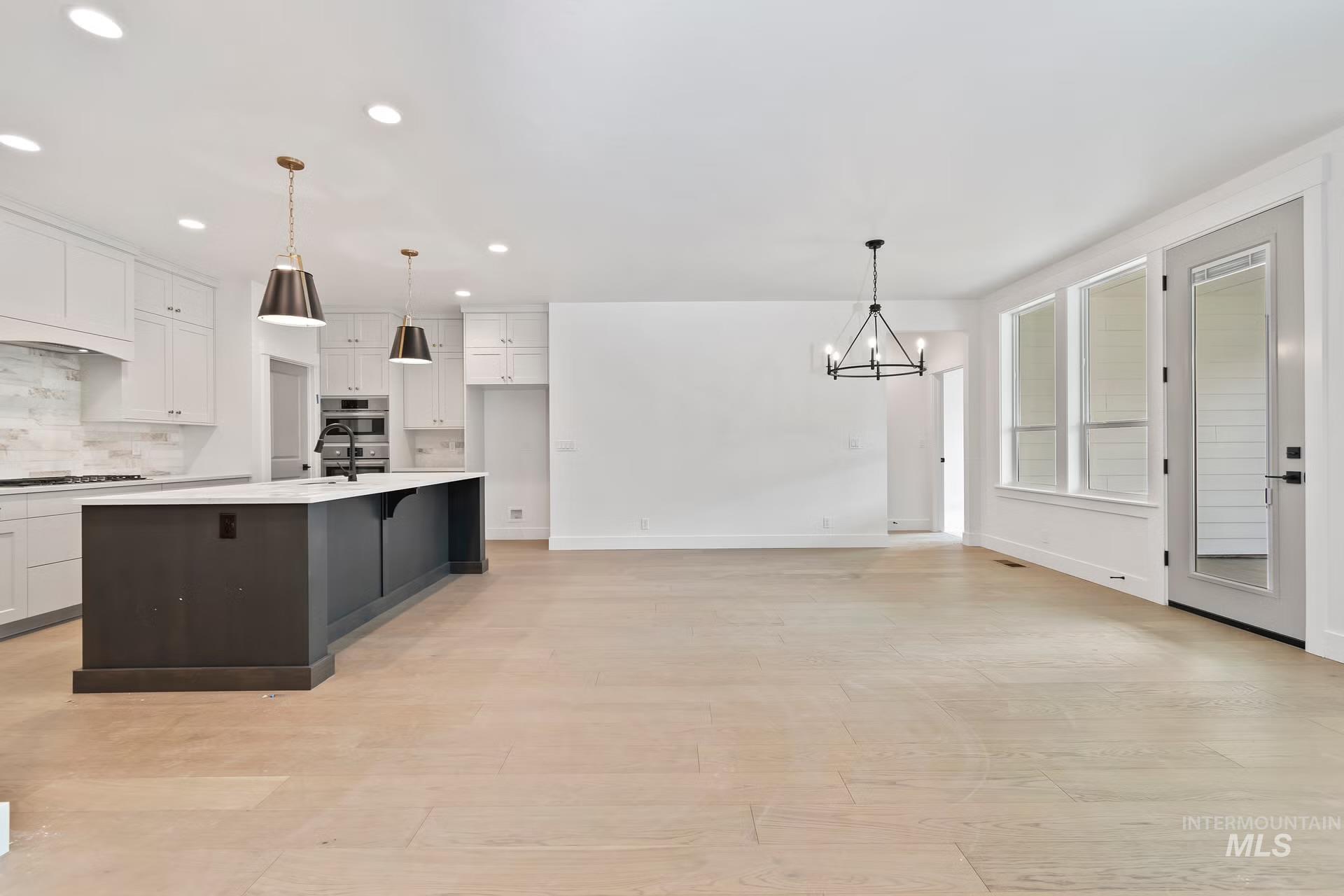 Kitchen with white cabinets, backsplash, an island with sink, light wood-style floors, and recessed lighting