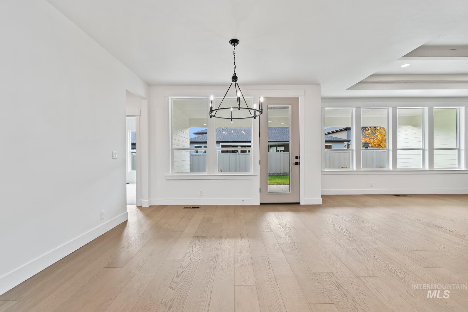 Unfurnished dining area featuring a chandelier, light wood finished floors, a tray ceiling, and recessed lighting