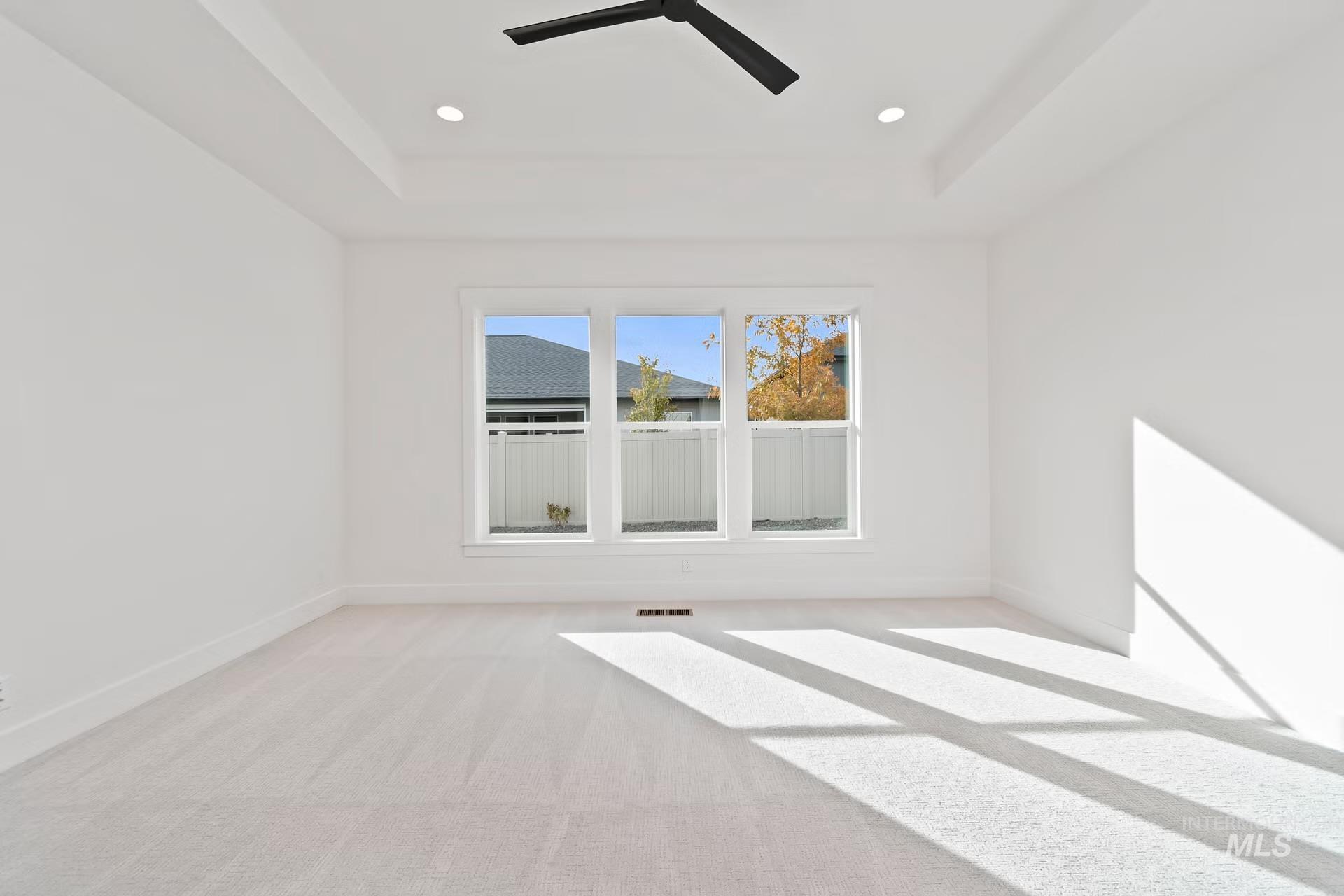 Empty room with a tray ceiling, light carpet, recessed lighting, and a ceiling fan