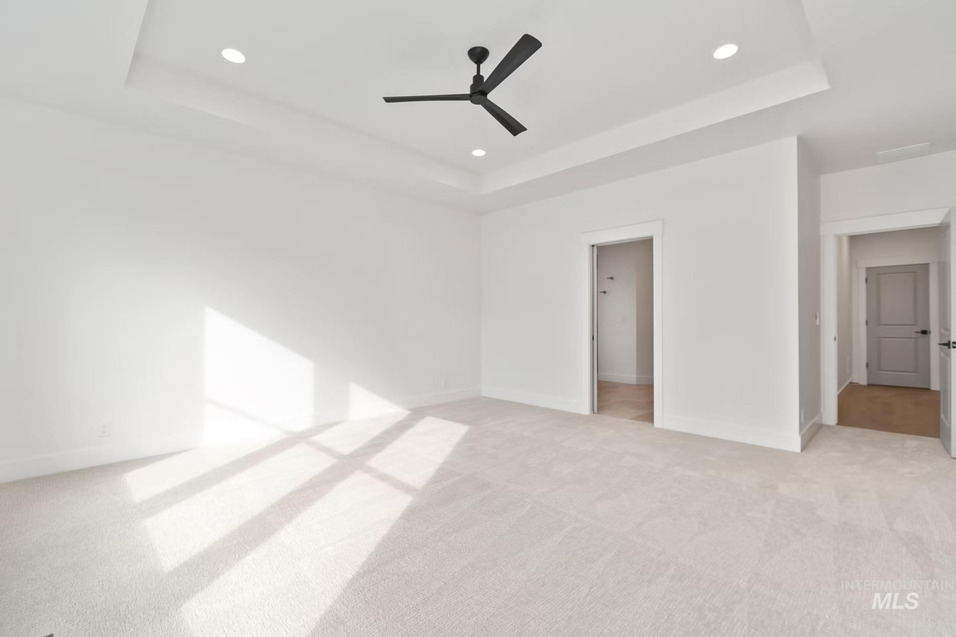 Unfurnished bedroom featuring a raised ceiling, light colored carpet, a ceiling fan, and recessed lighting