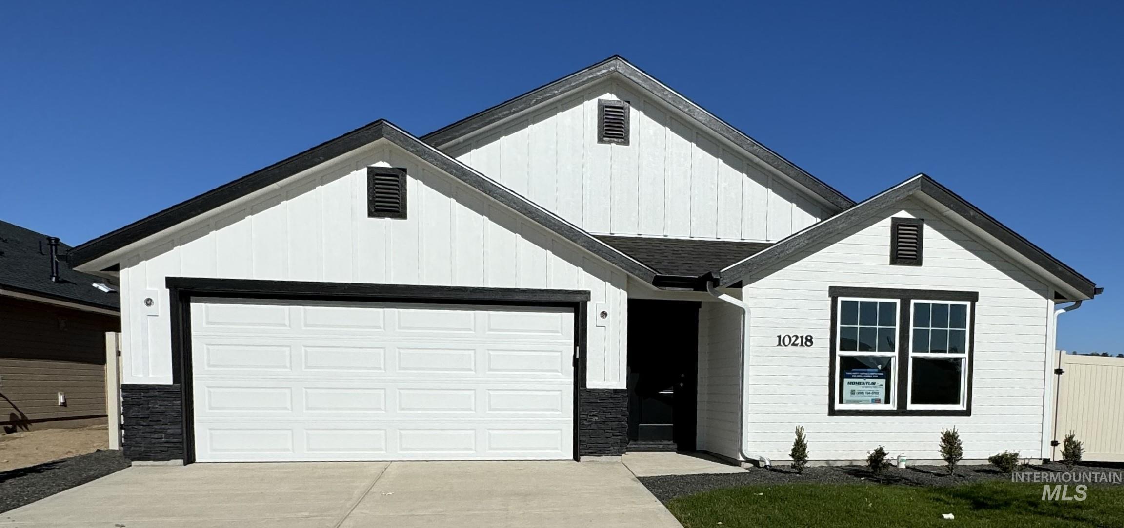 Modern farmhouse featuring board and batten siding, driveway, an attached garage, and stone siding