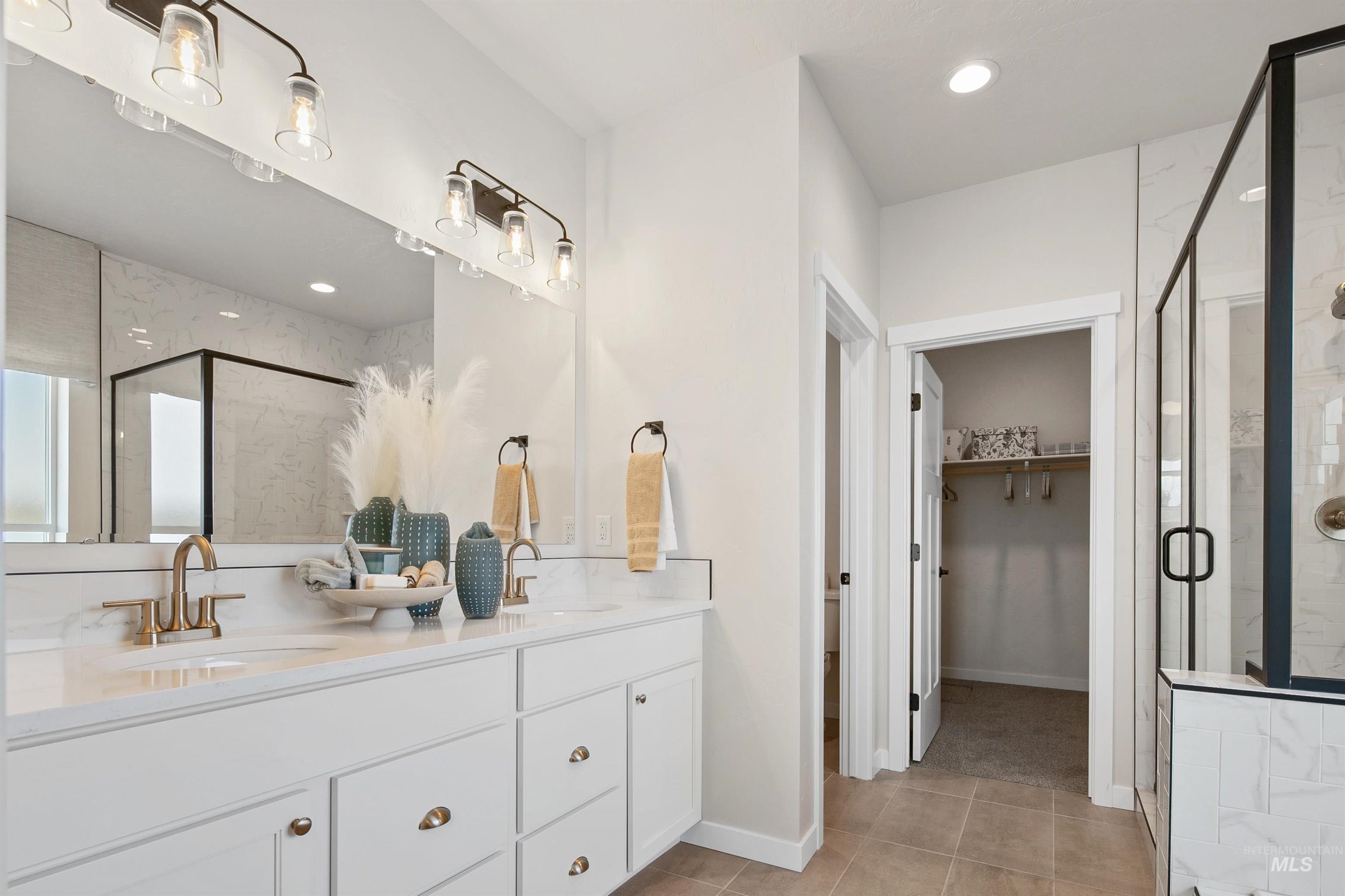 Bathroom with a marble finish shower, a spacious closet, double vanity, light tile patterned floors, and recessed lighting