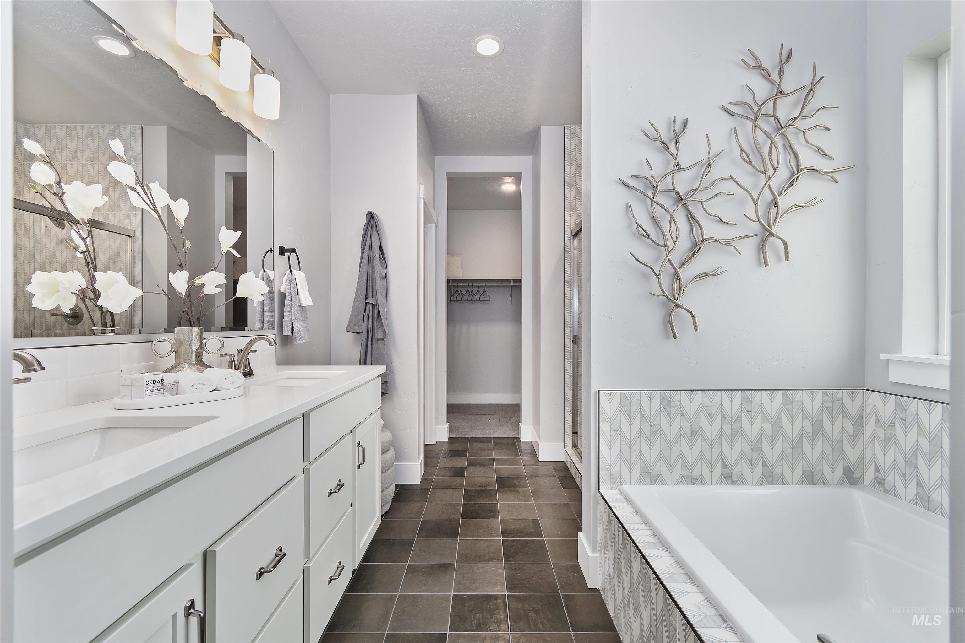 Bathroom featuring double vanity, a spacious closet, a garden tub, dark tile patterned flooring, and a shower stall