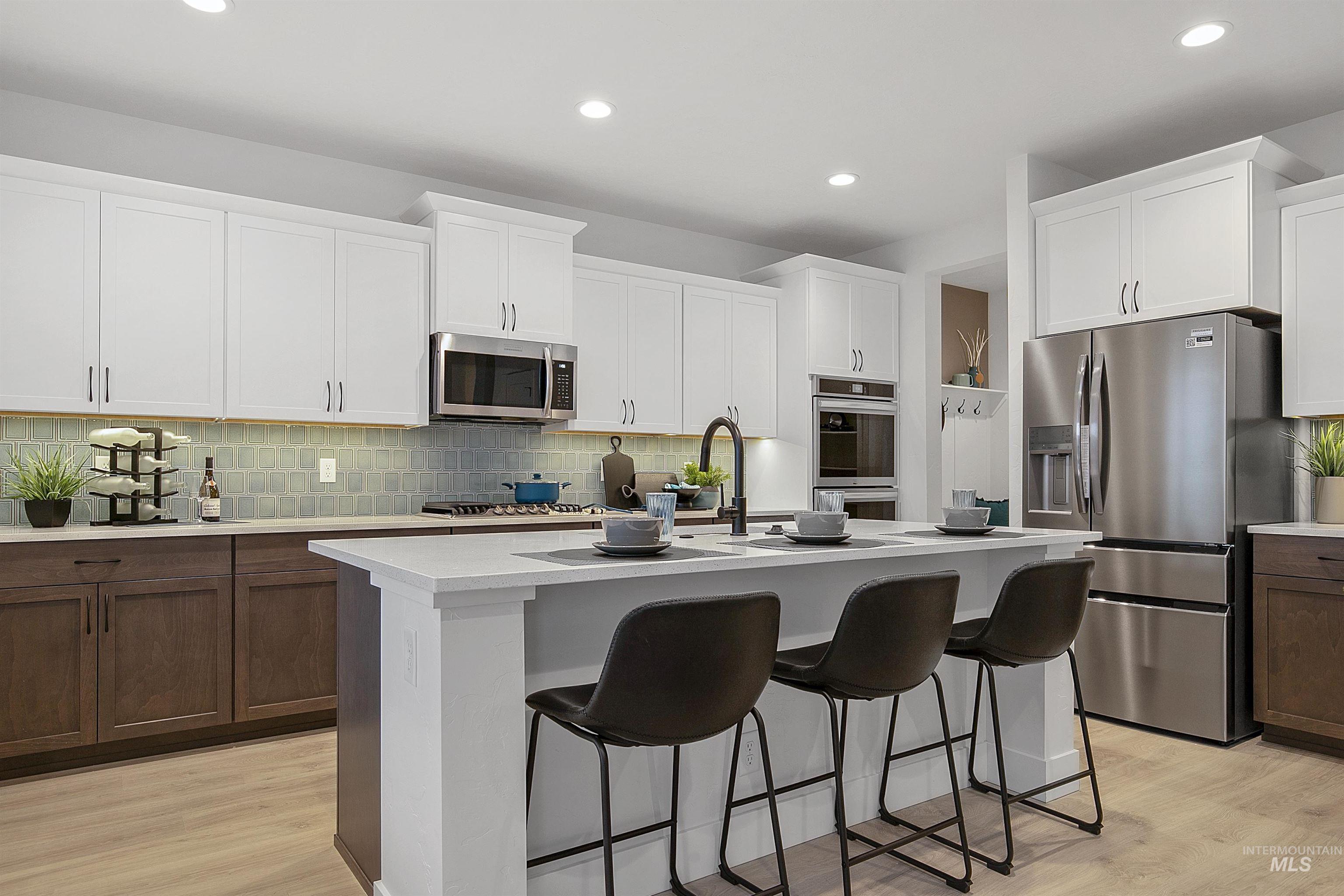 Kitchen with decorative backsplash, appliances with stainless steel finishes, light wood finished floors, white cabinetry, and recessed lighting