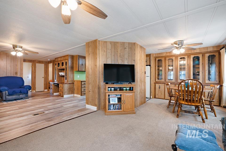 Living area with a ceiling fan, wooden walls, and light colored carpet