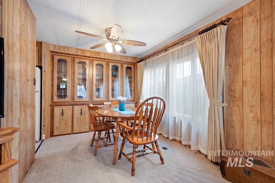 Dining area with wood walls, light colored carpet, and a ceiling fan