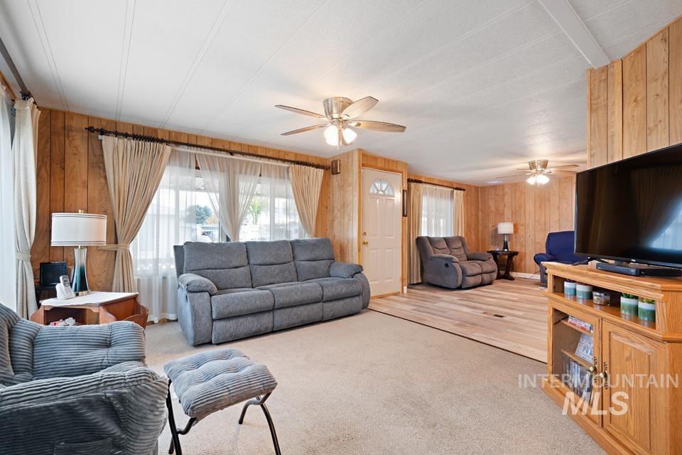 Carpeted living room with wooden walls and ceiling fan