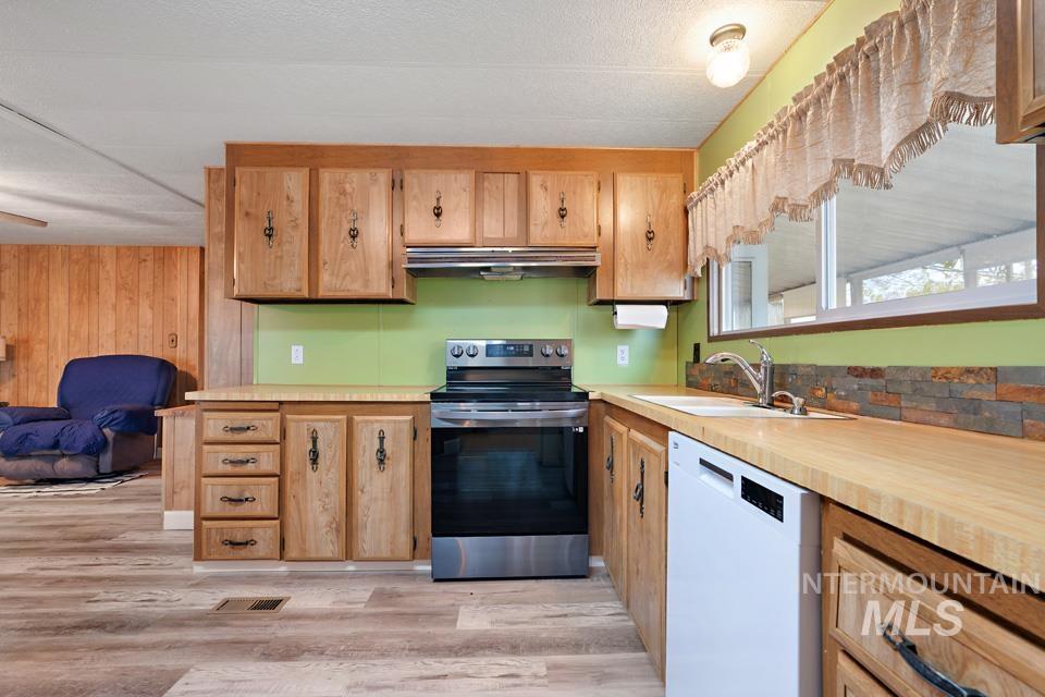 Kitchen with stainless steel range with electric stovetop, light countertops, dishwasher, light wood-style flooring, and wooden walls