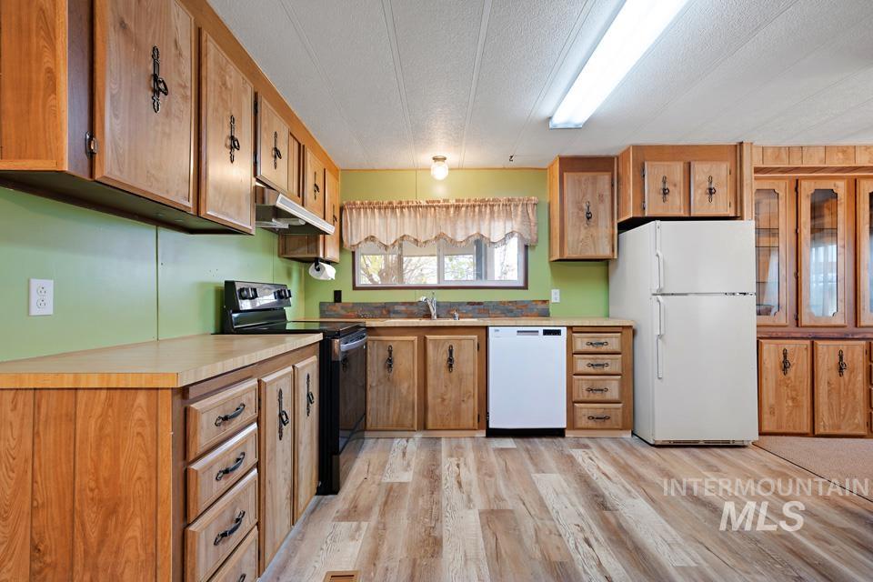 Kitchen featuring white appliances, light wood-style floors, light countertops, under cabinet range hood, and a textured ceiling