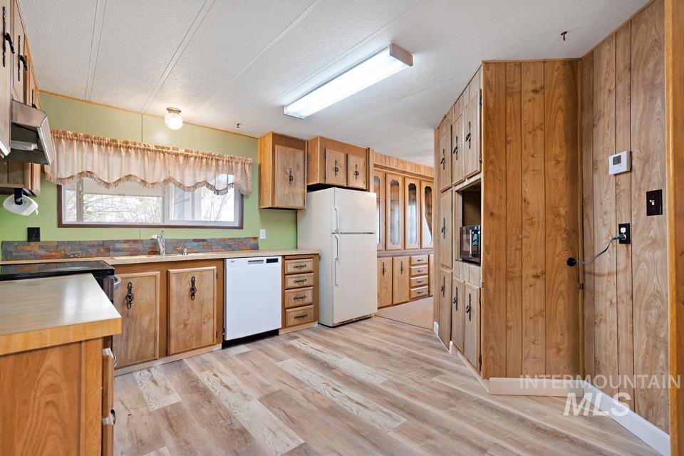 Kitchen featuring white appliances, light countertops, light wood finished floors, brown cabinets, and a textured ceiling