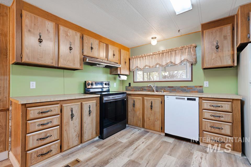 Kitchen with stainless steel electric range oven, white dishwasher, light countertops, under cabinet range hood, and light wood-type flooring