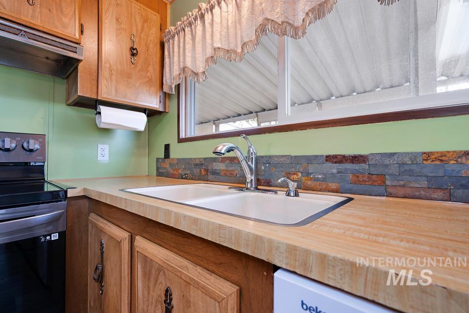Kitchen featuring electric range, under cabinet range hood, light countertops, and brown cabinetry
