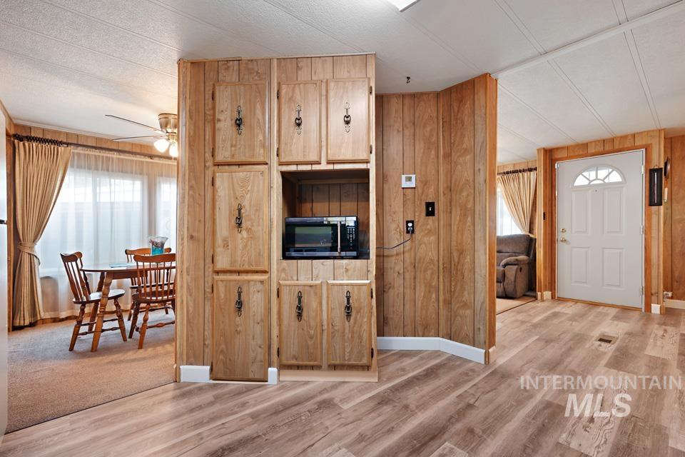 Kitchen with wooden walls, a ceiling fan, stainless steel microwave, and light wood-style floors