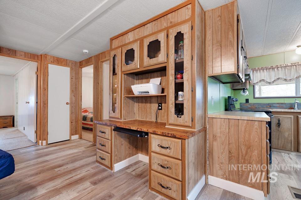 Kitchen featuring light brown cabinetry, wooden walls, light wood-style floors, range with electric cooktop, and glass insert cabinets