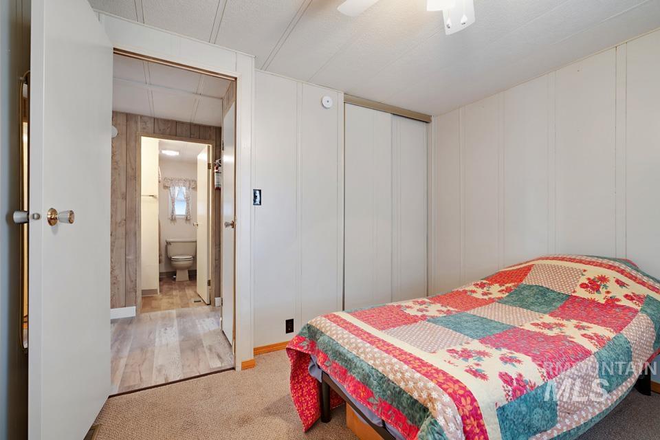 Bedroom with light colored carpet, a decorative wall, a closet, ceiling fan, and light wood-type flooring