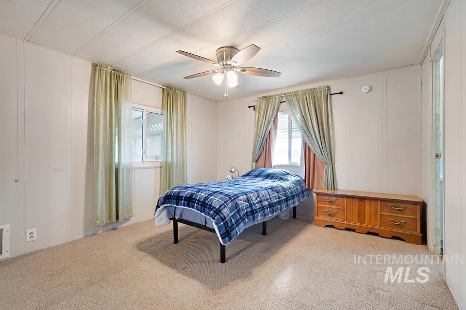 Carpeted bedroom featuring ceiling fan and a decorative wall