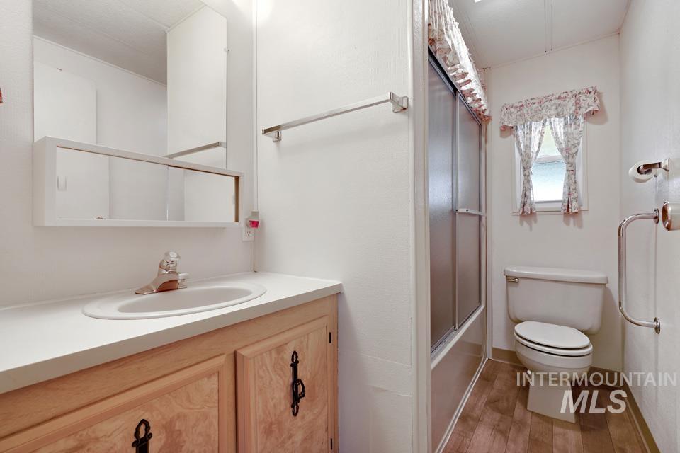 Bathroom with light wood-type flooring, vanity, and shower / bath combination with glass door