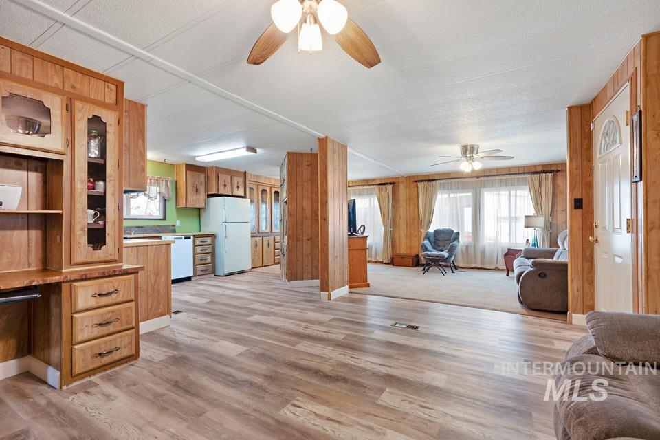 Kitchen with open floor plan, light wood-style flooring, white appliances, wooden walls, and brown cabinetry