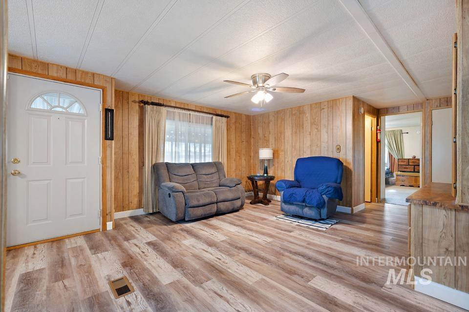 Living room with wooden walls, light wood-style floors, and ceiling fan
