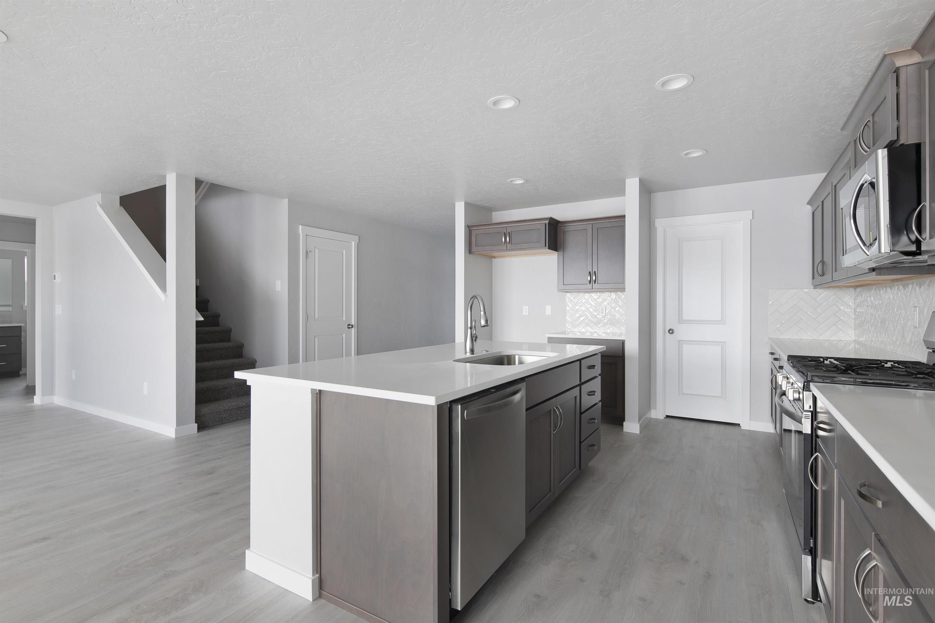 Kitchen featuring stainless steel appliances, tasteful backsplash, light wood-style flooring, a center island with sink, and a textured ceiling