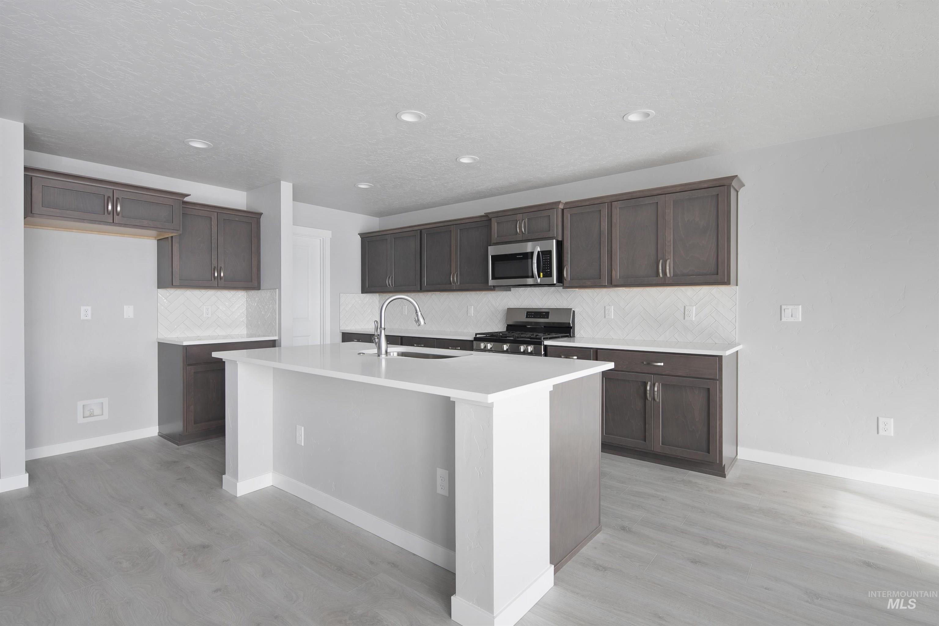 Kitchen featuring backsplash, stainless steel appliances, dark brown cabinets, an island with sink, and recessed lighting