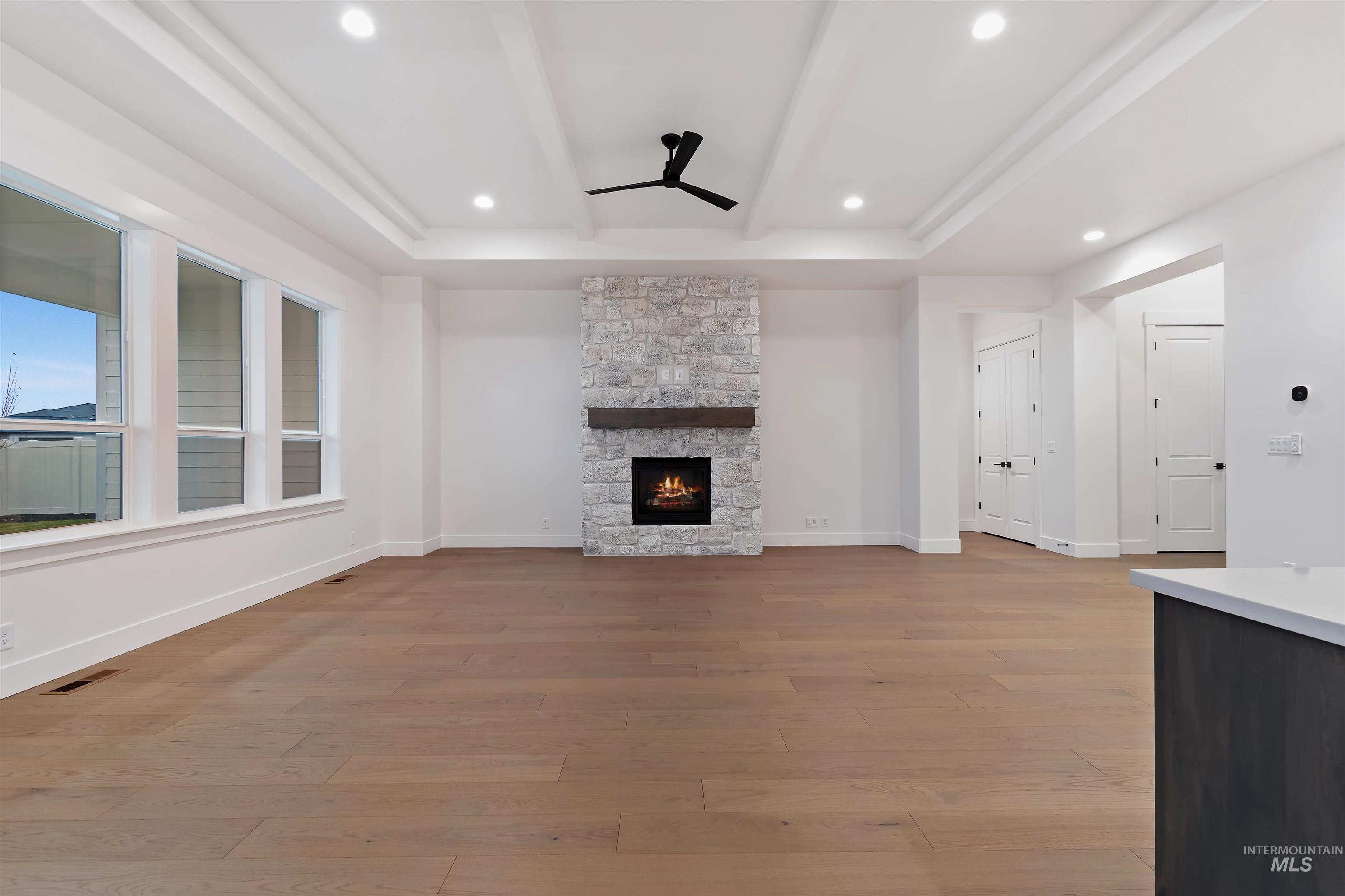 Unfurnished living room featuring a ceiling fan, a stone fireplace, light wood-style floors, beamed ceiling, and recessed lighting