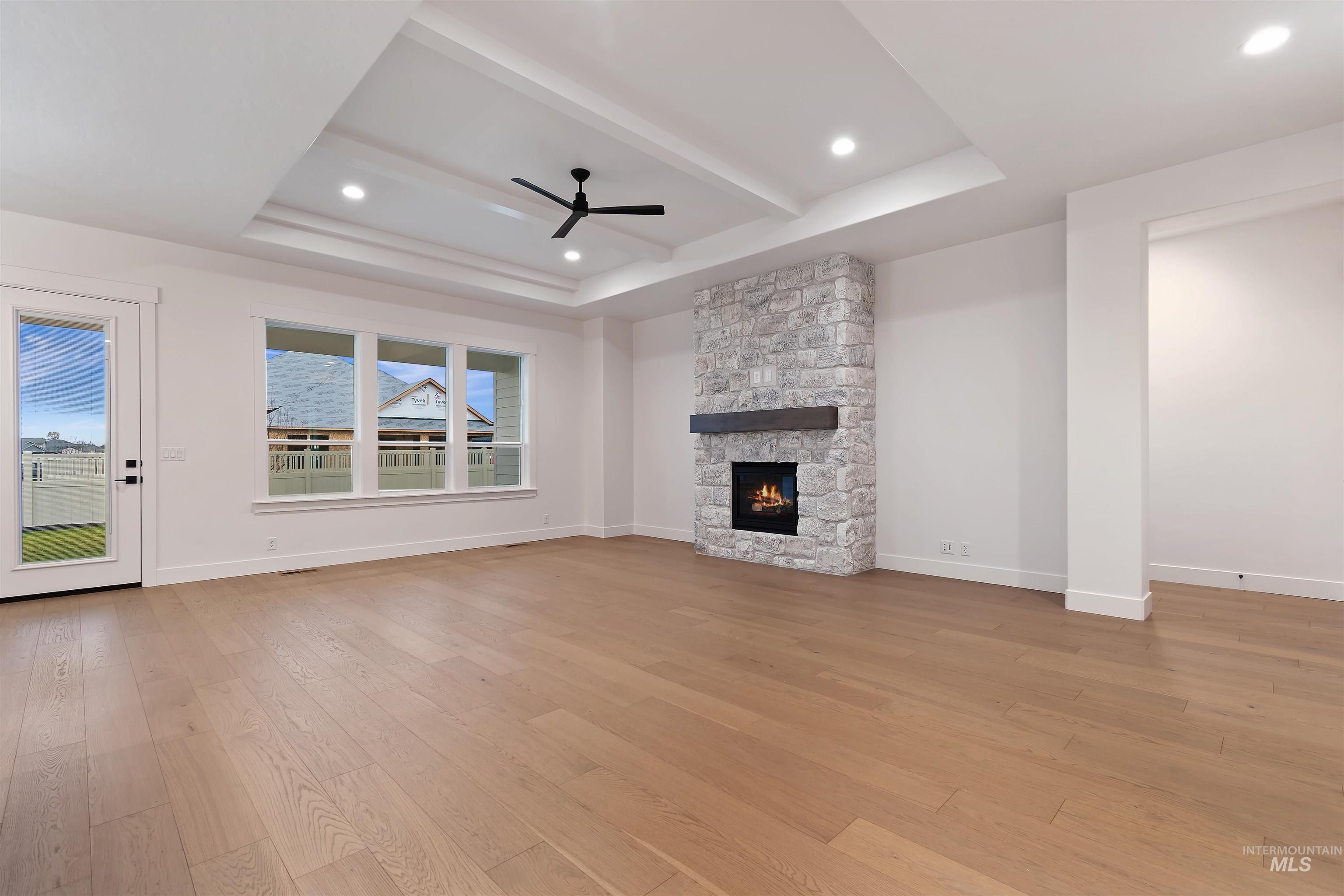 Unfurnished living room featuring light wood finished floors, ceiling fan, recessed lighting, a fireplace, and a raised ceiling