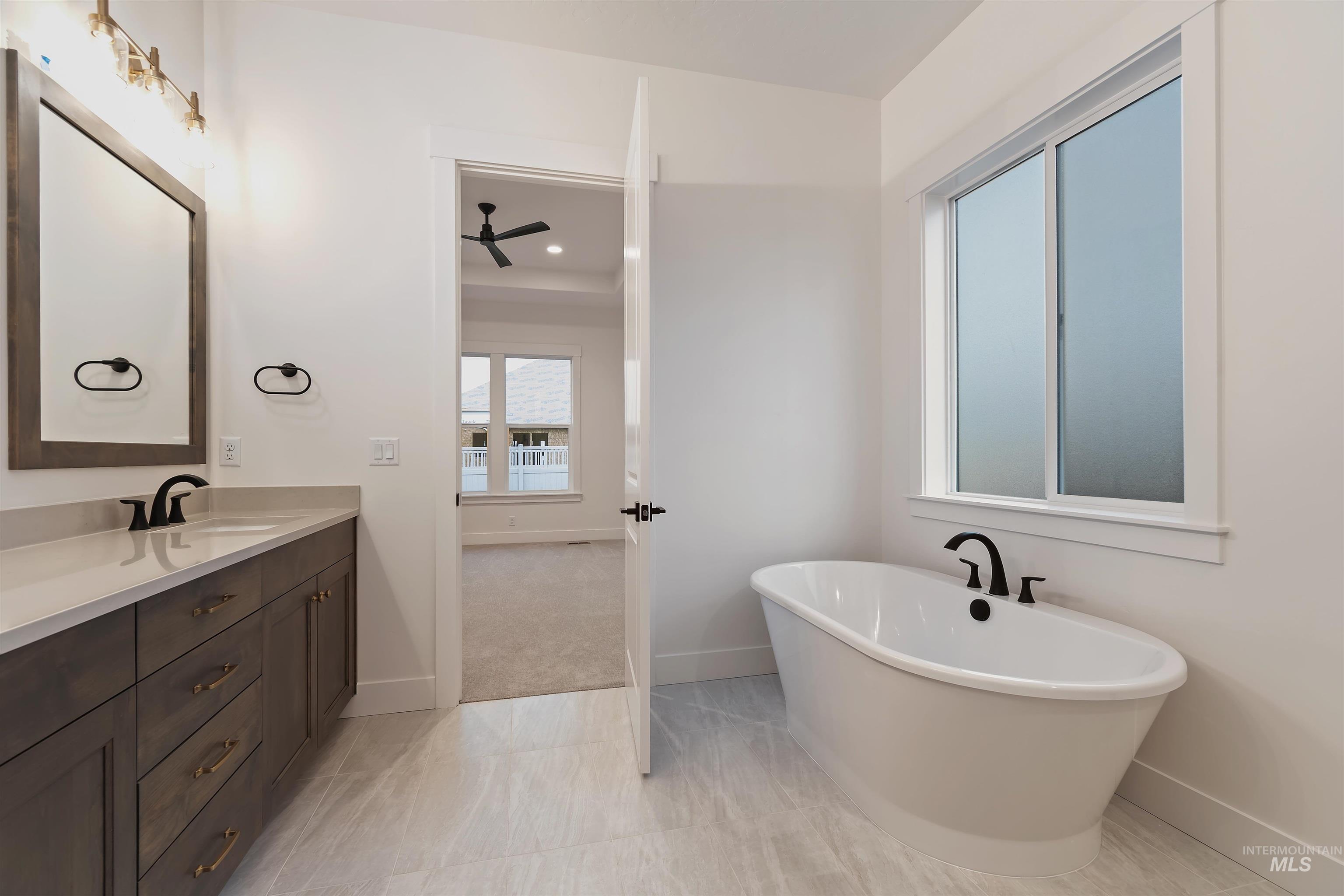 Full bath with a freestanding bath, vanity, a ceiling fan, and light tile patterned floors