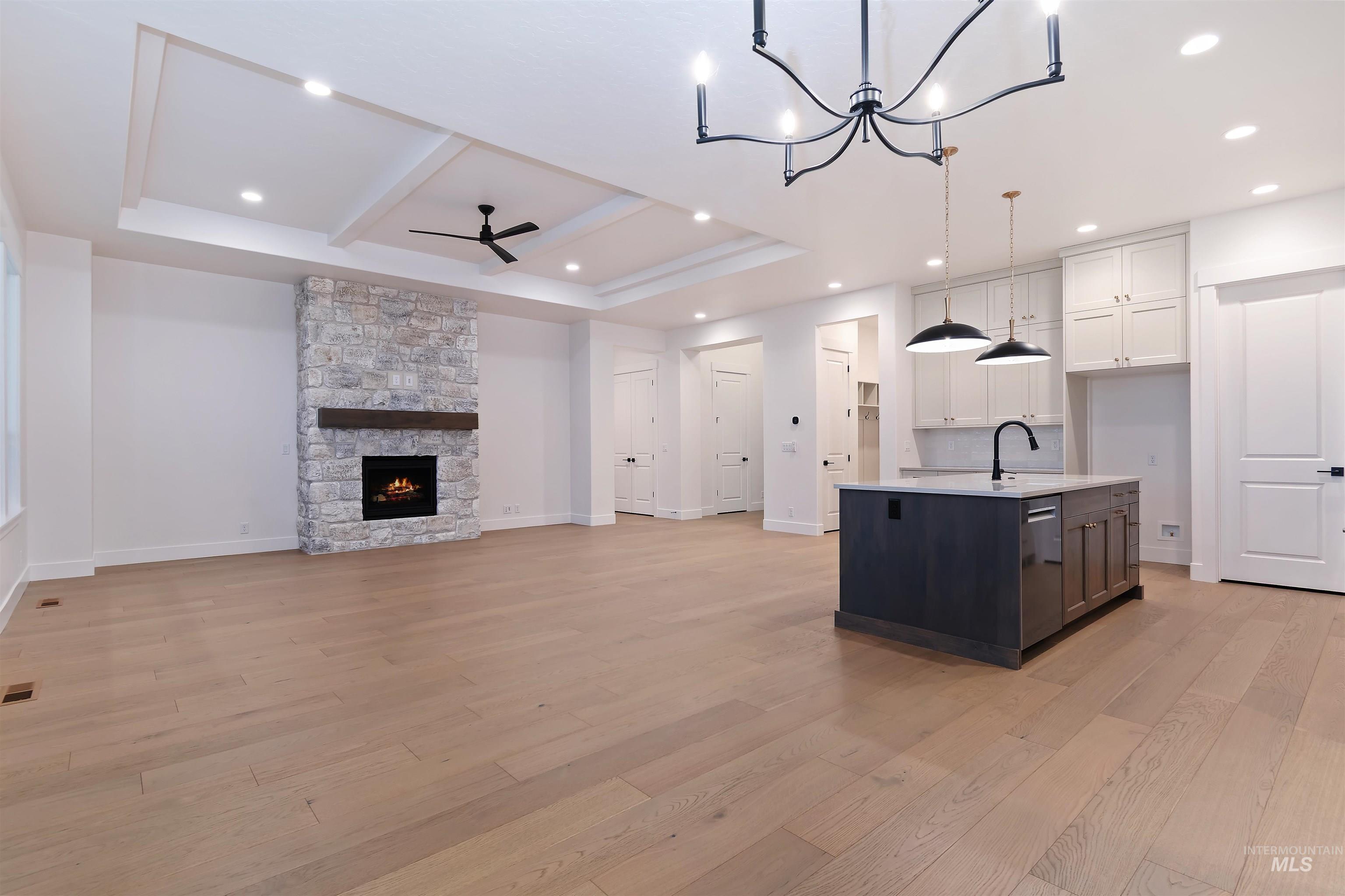 Kitchen featuring open floor plan, a tray ceiling, hanging light fixtures, a center island with sink, and light wood-type flooring