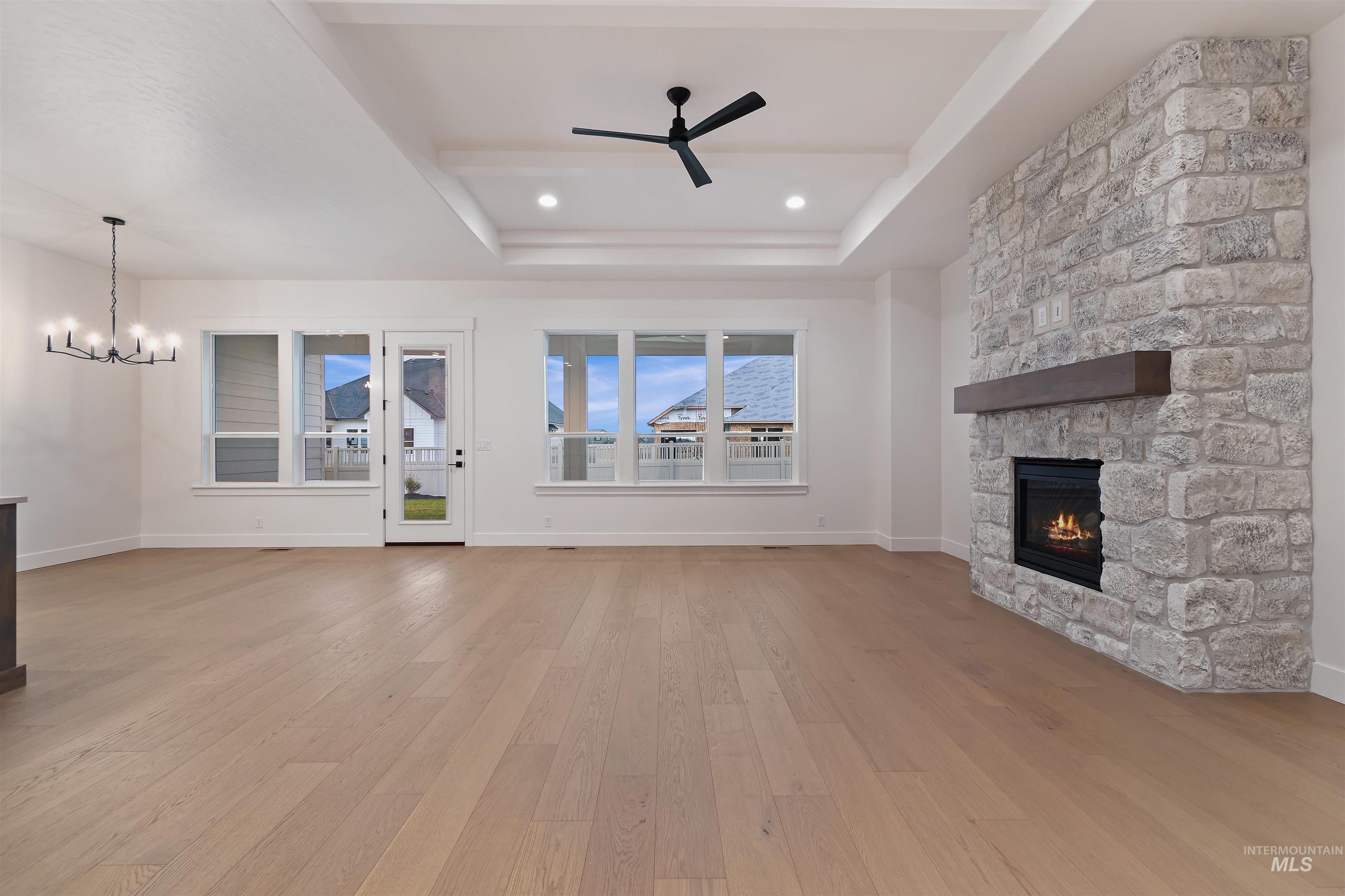 Unfurnished living room with a fireplace, a tray ceiling, light wood-type flooring, a ceiling fan, and recessed lighting