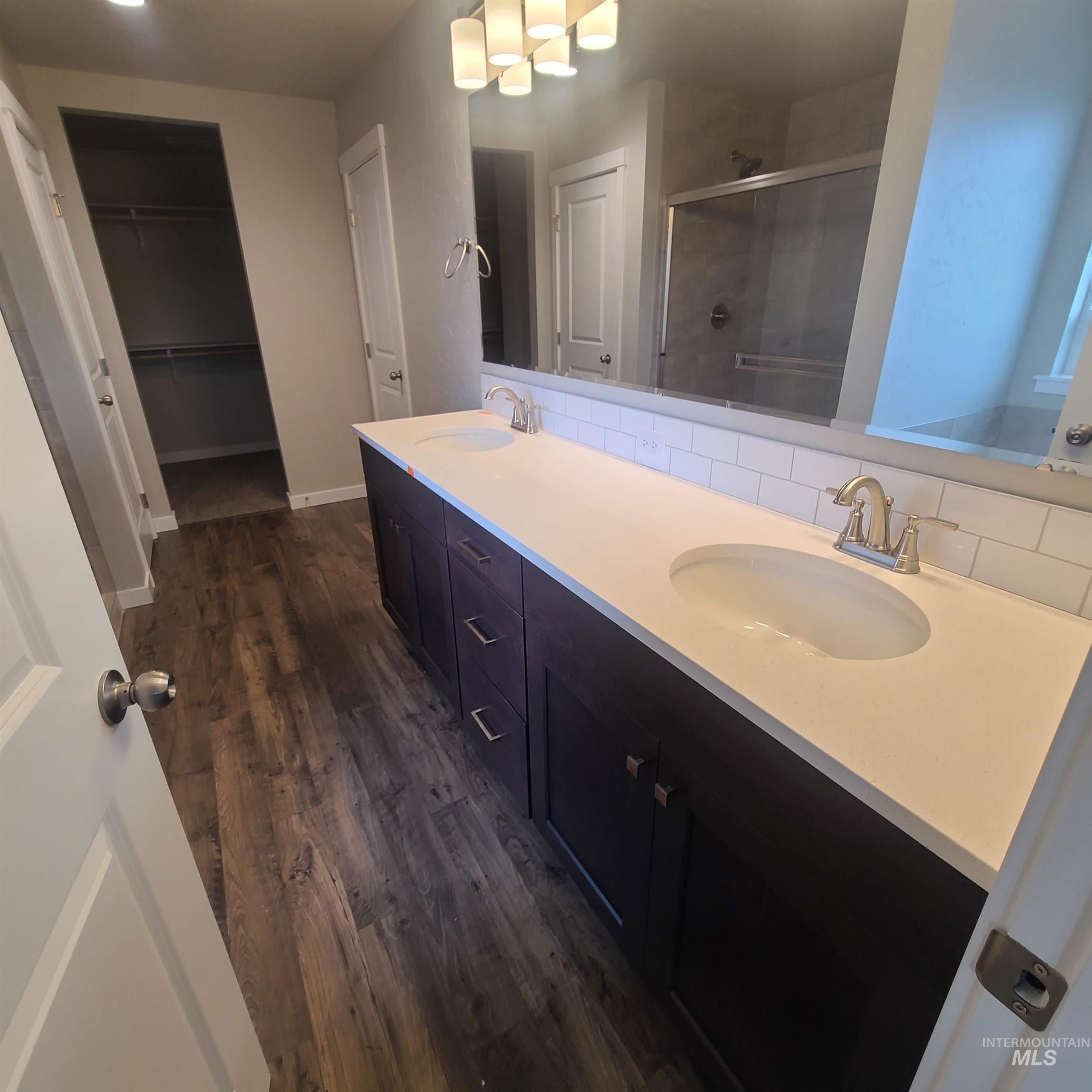 Bathroom with dark wood-style floors, double vanity, a walk in closet, a stall shower, and backsplash