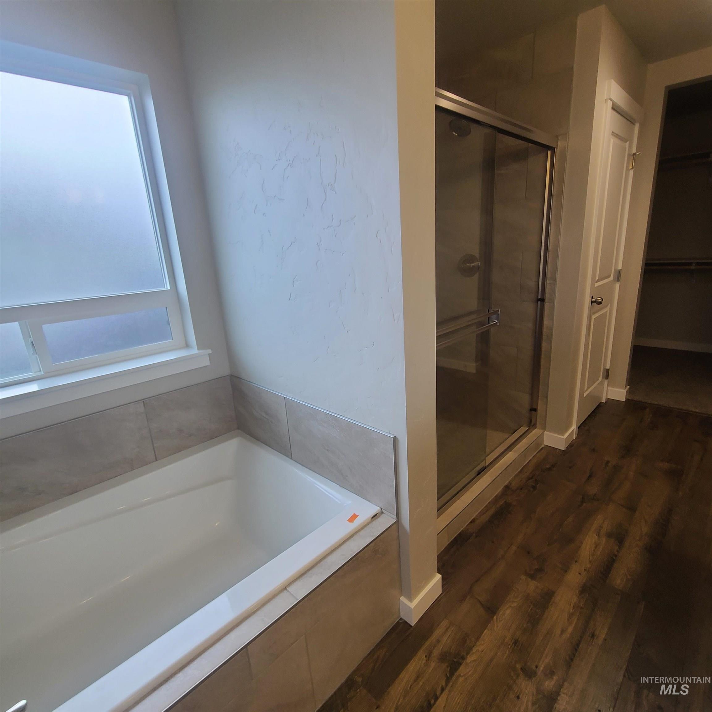 Bathroom with a stall shower, a garden tub, dark wood-type flooring, and a walk in closet