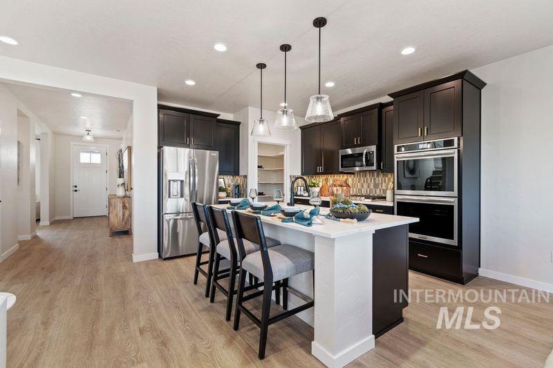 Kitchen featuring decorative backsplash, a breakfast bar, appliances with stainless steel finishes, light wood-style flooring, and decorative light fixtures