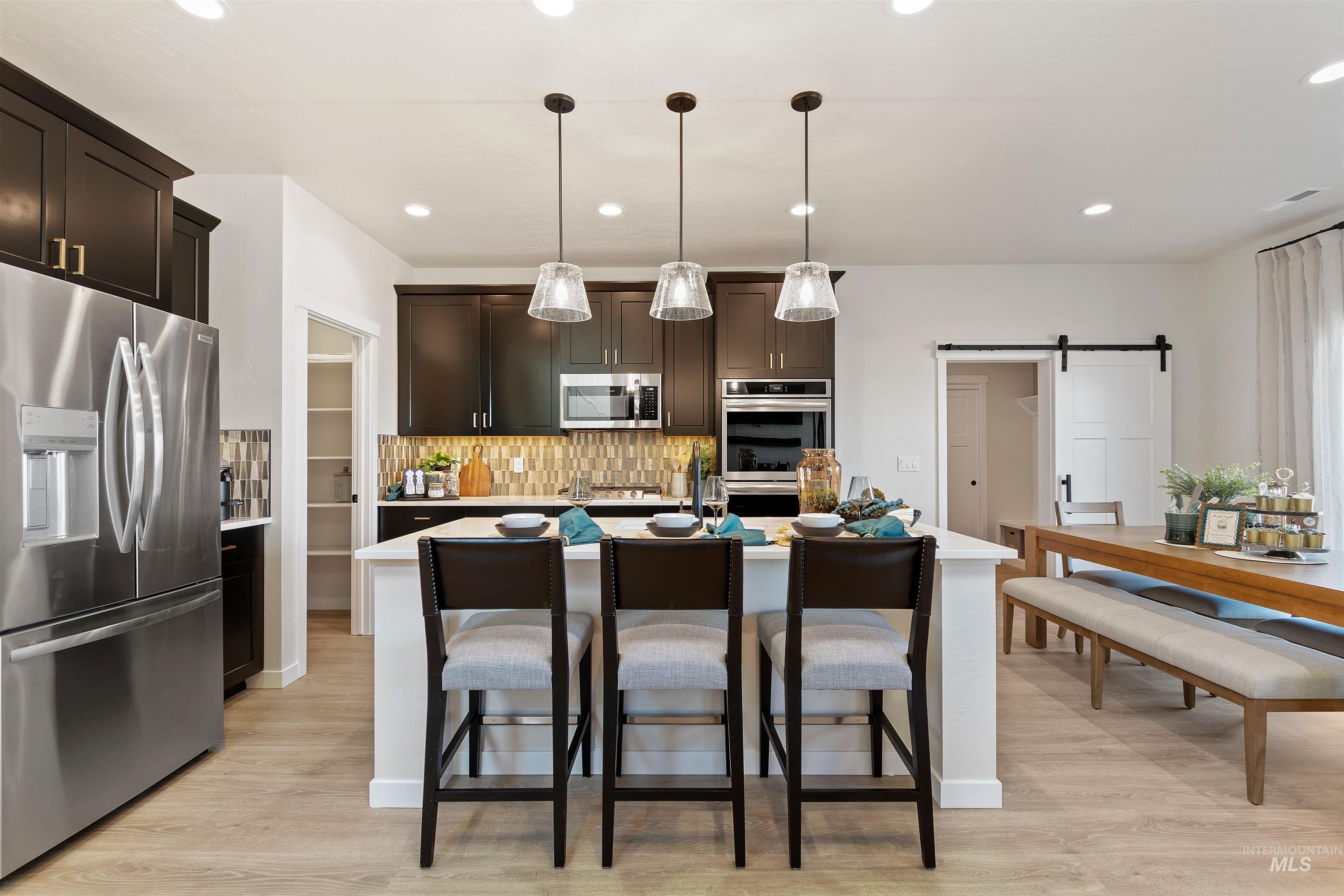 Kitchen with a barn door, dark brown cabinetry, stainless steel appliances, tasteful backsplash, and hanging light fixtures