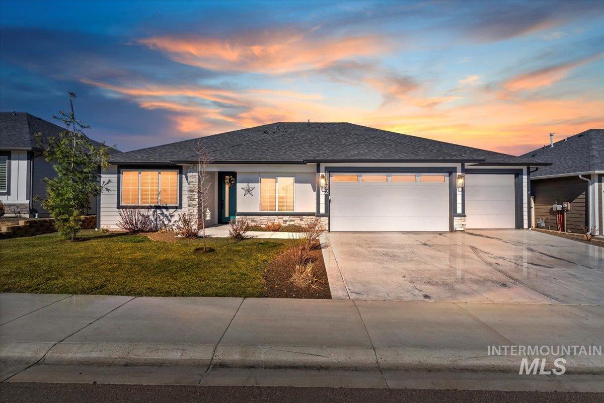 View of front facade with a garage, a shingled roof, concrete driveway, stone siding, and a front yard