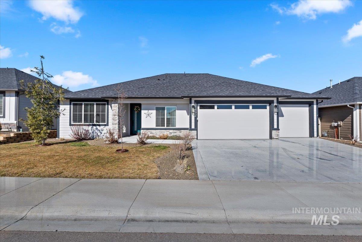 Single story home featuring stone siding, roof with shingles, driveway, an attached garage, and a front lawn
